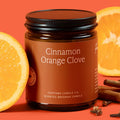 Cinnamon Orange Clove candle in a jar with oranges and cinnamon sticks on an orange background
