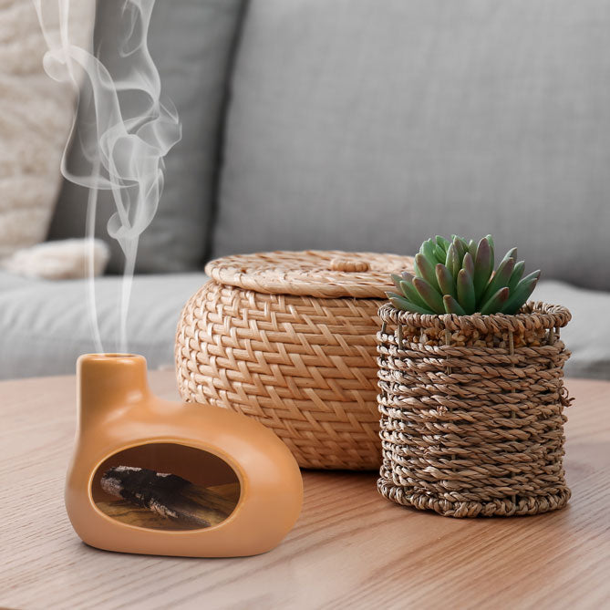 Ceramic Smudging-Hearths with smoke, woven basket, and small plant on a wooden surface.