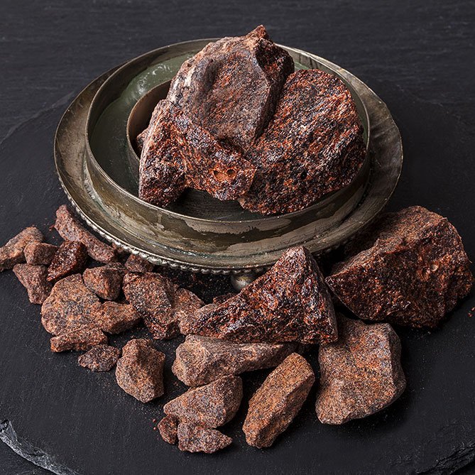 Rough dark reddish-brown mineral or stone chunks arranged on a round metal tray and scattered around it on a dark slate surface.