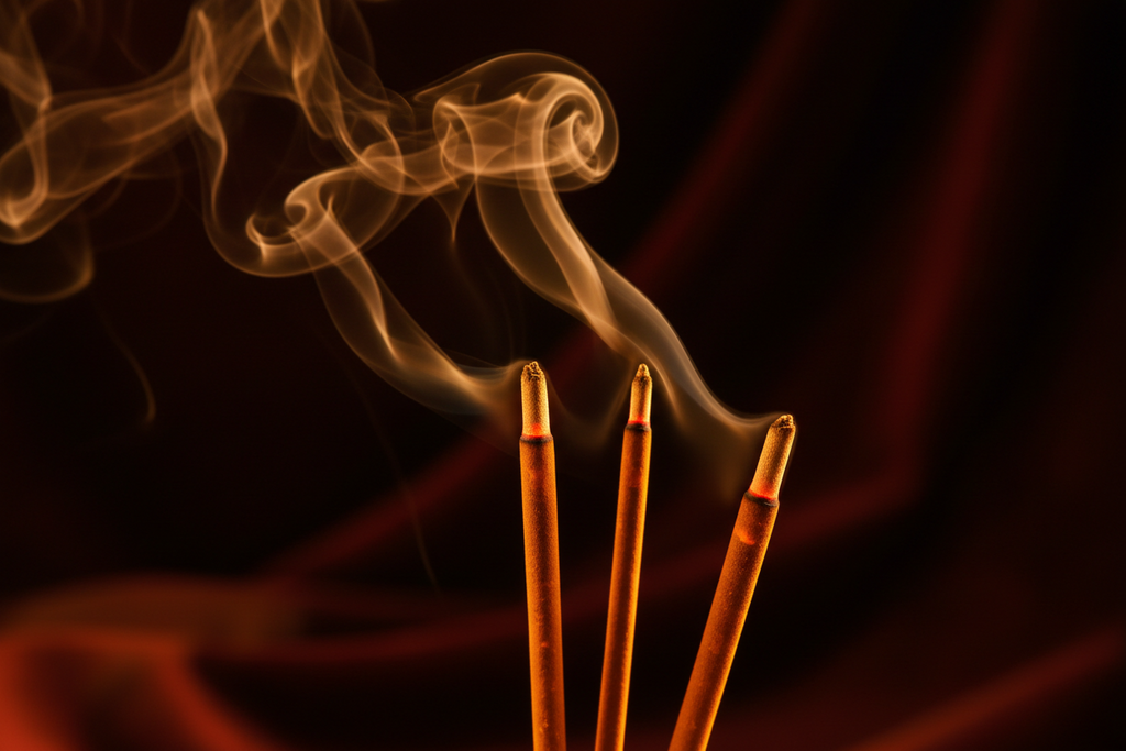 Three incense sticks with smoke against a dark background