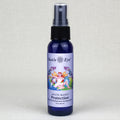 A 2.0 oz dark blue glass spray bottle of Sun's Eye 'Mystic Blends' 'Attraction' unscented and sweetened straight spray, featuring a black spray nozzle and a colorful label with a fairy illustration, set against a neutral light gray textured background.