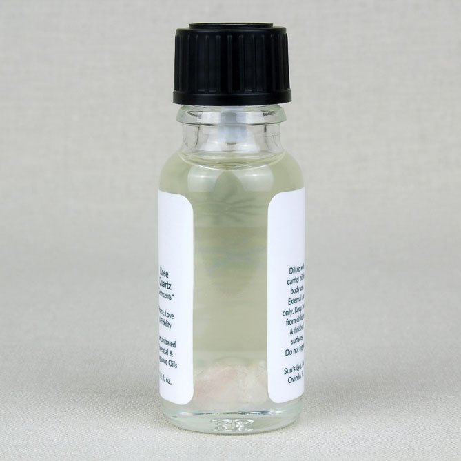Small glass bottle with a black cap filled with rose quartz oil on a light gray background