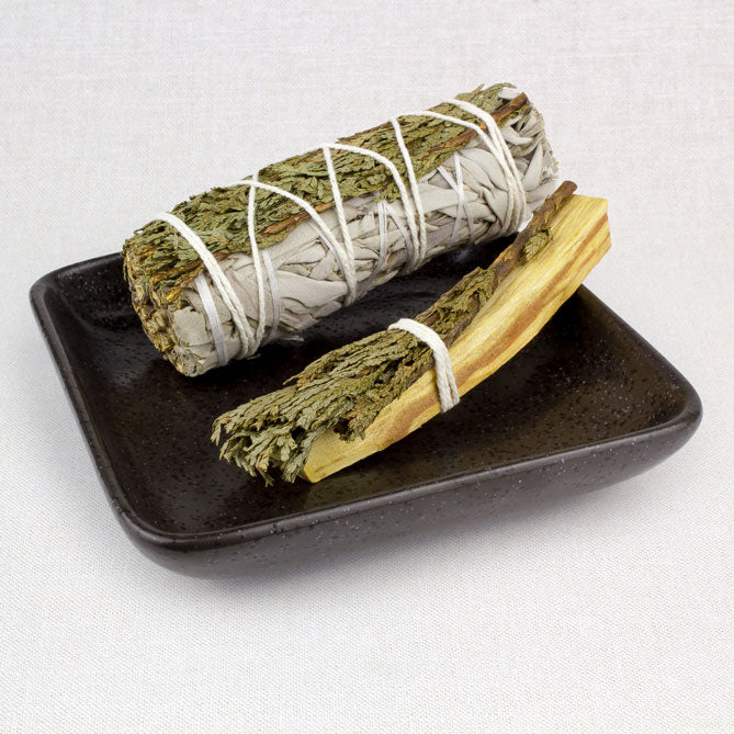 Two bundles of sage tied with twine on a black plate against a white background
