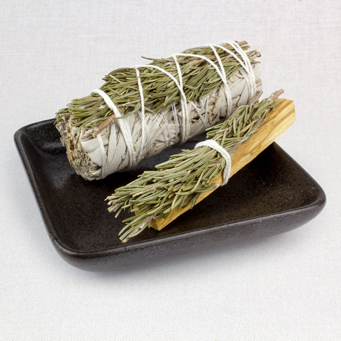 Two bundles of sage on a black plate against a light background